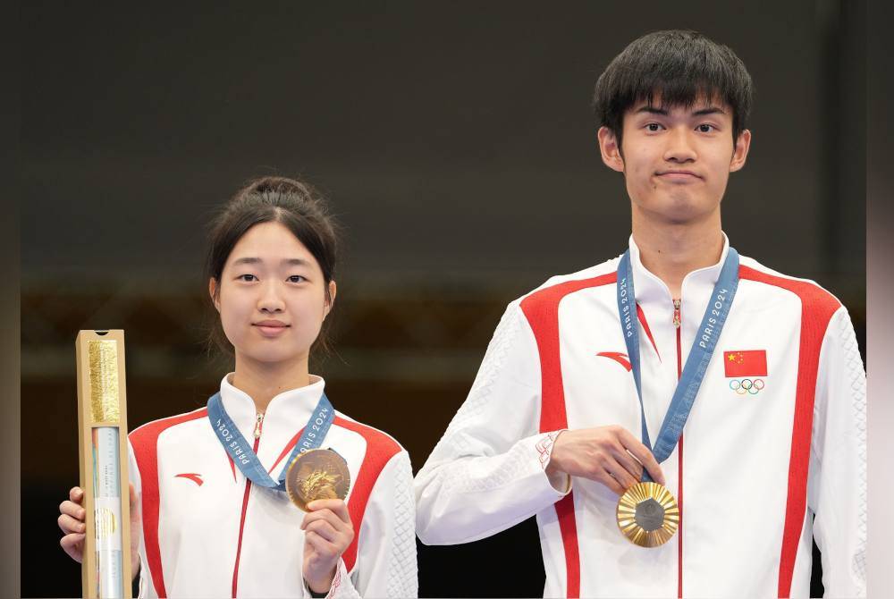 Huang Yuting dan Sheng Lihao di podium selepas memenangi emas acara 10m air rifle berpasukan campuran Paris 2024 di Pusat Menembak Kebangsaan Perancis, Chateauroux. Foto AFP