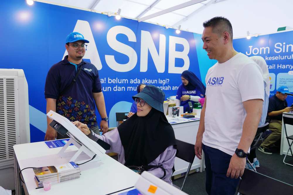Muzzaffar (kanan) melihat pengunjung menggunakan salah satu kiosk di reruai ASNB