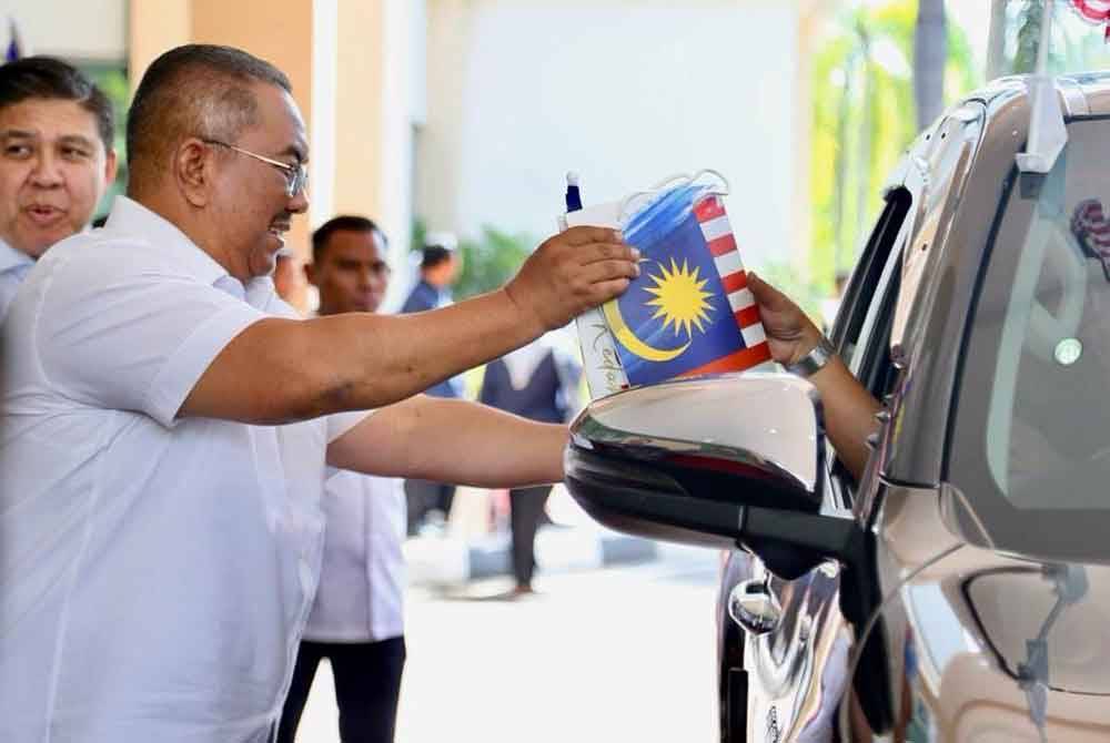 Muhammad Sanusi mengagihkan Jalur Gemilang kepada peserta konvoi.