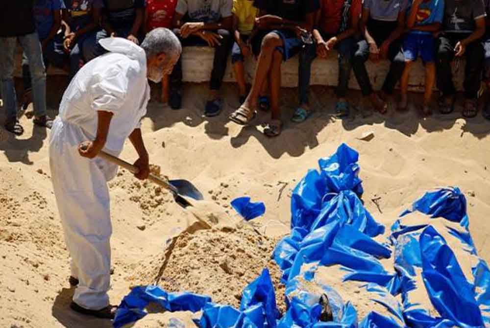 Seorang individu mengebumikan mayat-mayat rakyat Palestin tanpa identiti di sebuah kubur besar selepas mayat-mayat tersebut diserahkan semula oleh tentera Israel. - Gambar REUTERS