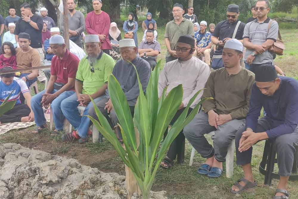 Bapa mangsa, Mohd Azril Kamarudin (duduk dua dari kanan), 35, membaca talkin selepas arwah anaknya dikebumikan di Tanah Perkuburan Islam Kampung Teluk Piai di sini pada Rabu.