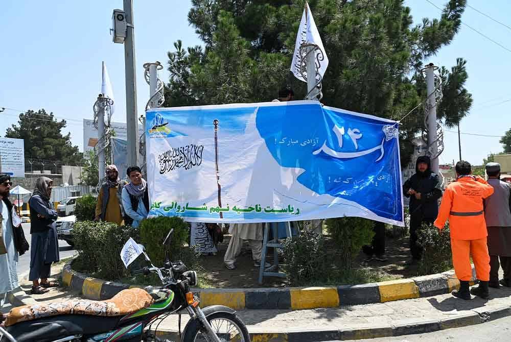 Pekerja perbandaran memasang kain rentang mengenai sambutan ulang tahun ketiga pengusiran AS dari Afghanistan di persimpangan jalan raya di sekitar Kabul.