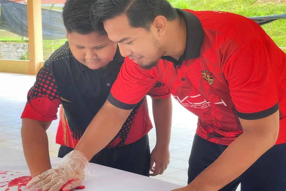 Seorang pelajar sedang mengecap telapak tangan pada Jalur Gemilang sambil dibantu oleh gurunya.