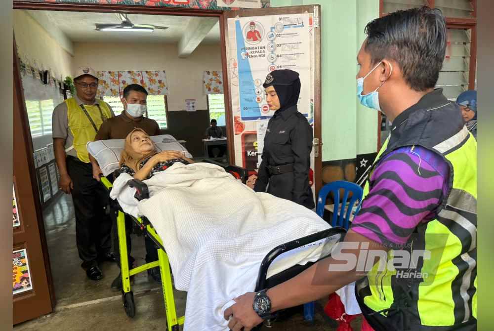 Wan Ropiah (tengah) yang berada di atas katil hospital ditolak masuk bilik mengundi.