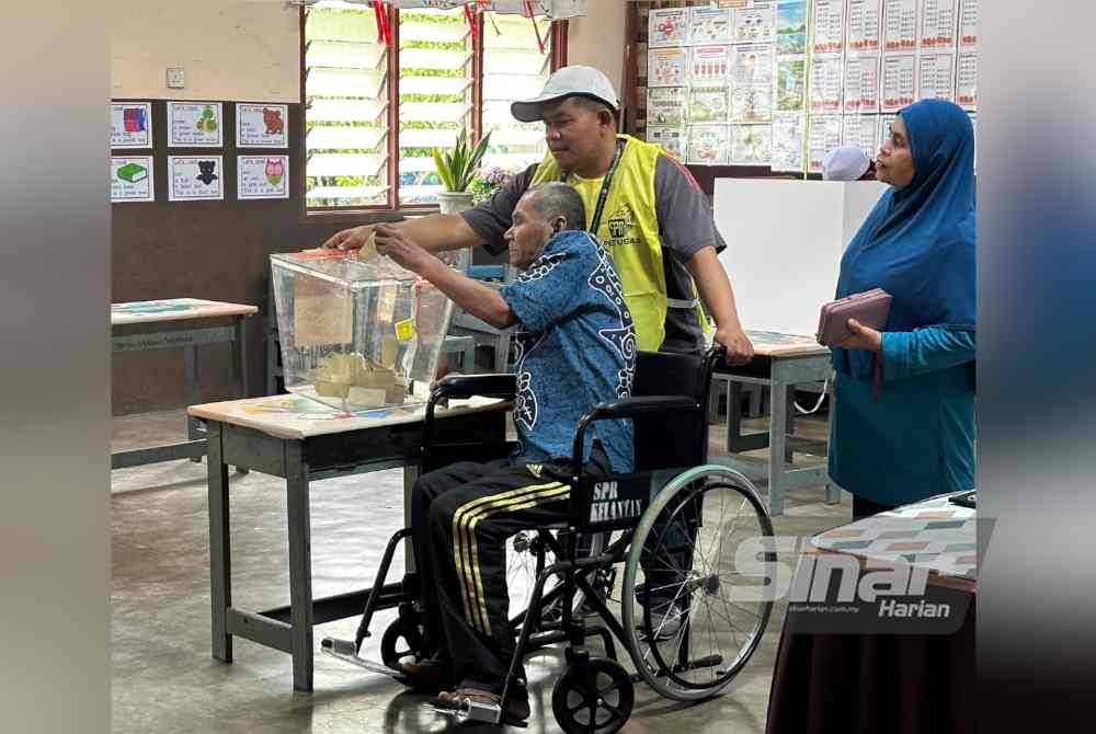 Mohd Yusof (kiri) memasukkan kertas undi ke dalam kotak selepas selesai memilih pada PRK DUN Nenggiri pada Sabtu.