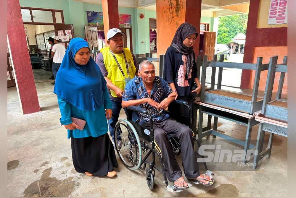 Mohd Yusof (tengah) berkerusi roda ketika dibawa ke pusat mengundi di SK Jeram Tekoh, Gua Musang.