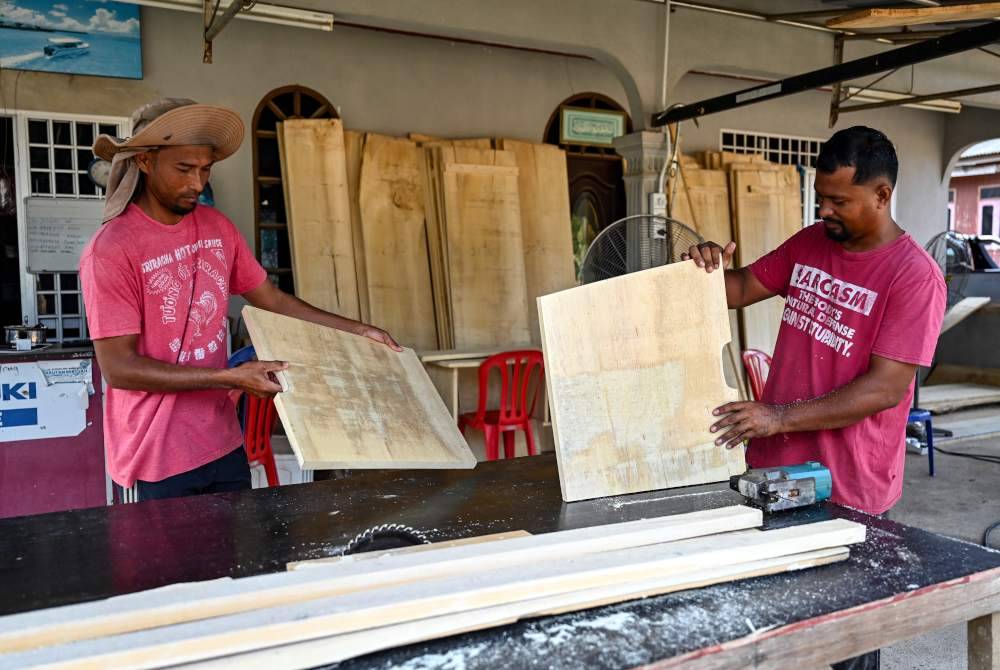 Anuar Abdullah bersama Maridwan (kanan) melakukan kerja-kerja memotong papan untuk membuat keranda. Foto Bernama