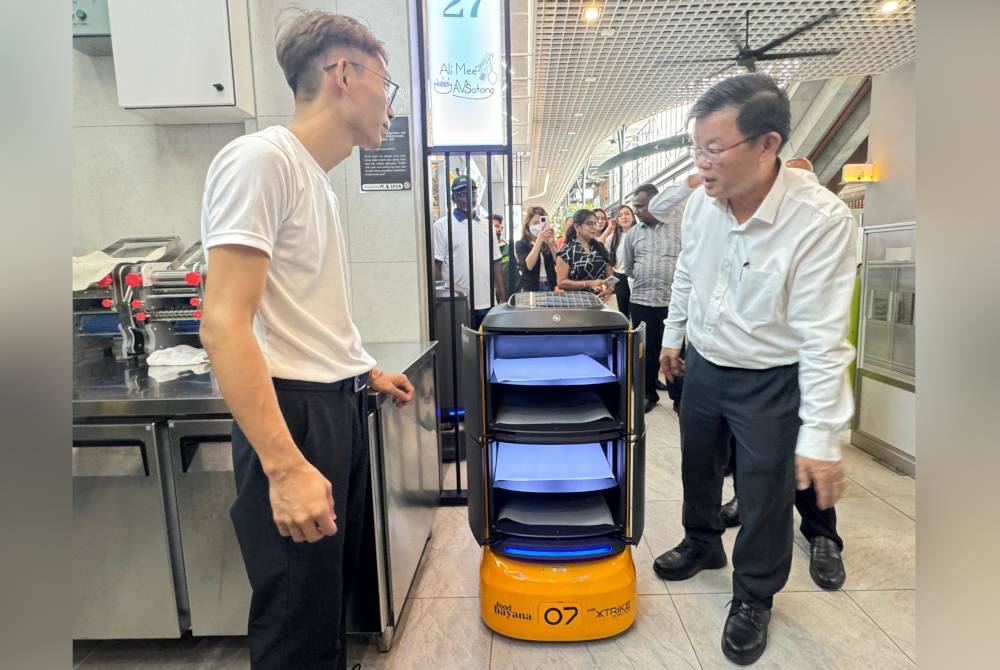 Kon Yeow (kanan) mendengar penerangan daripada salah seorang peniaga di Food Bayana mengenai fungsi robot di pusat makanan tersebut.