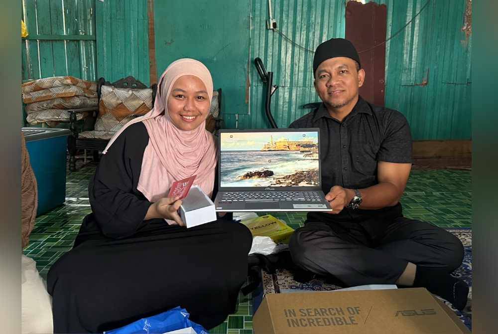 Noor Farra Wahida (kiri) menerima sumbangan komputer riba daripada Raja Shamri (kanan).