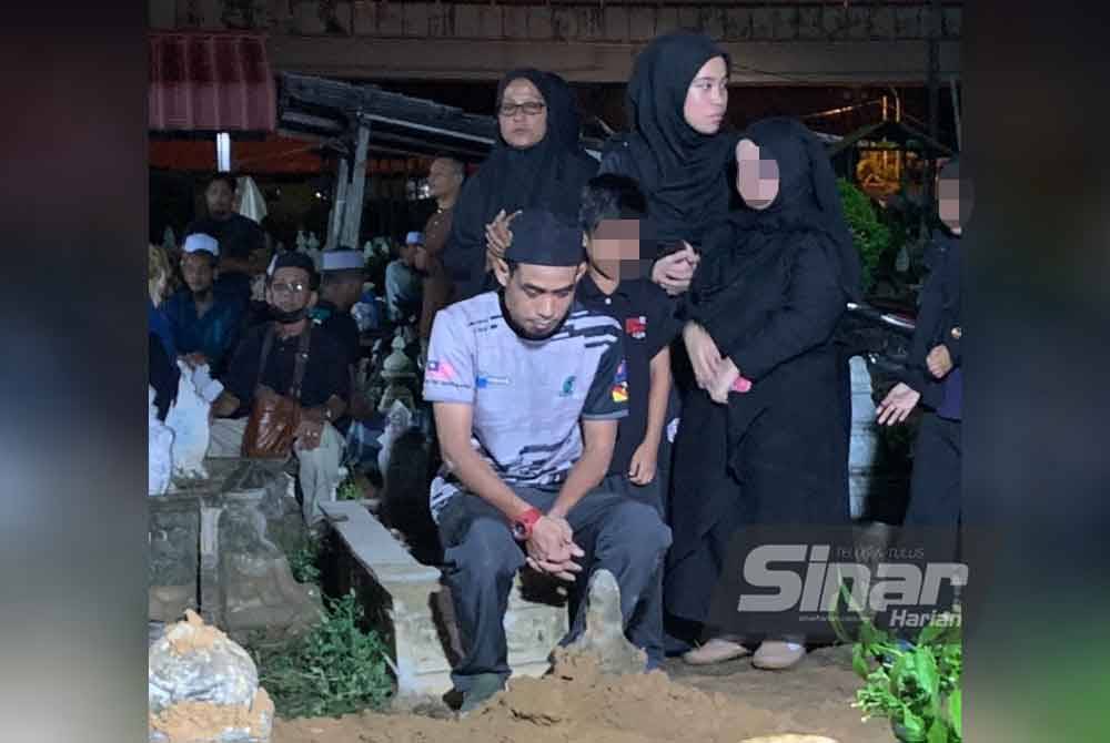 Mohd Yusof (tengah) yang masih sugul duduk di hadapan kubur Istiqomah selepas selesai jenazah dikebumikan.