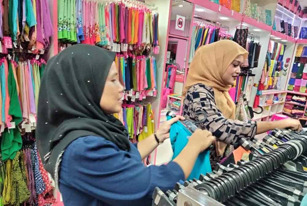 Che Morniza (kiri) menyusun pakaian di kedainya.