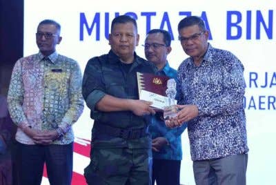 Saifuddin Nasution (kanan) menyampaikan hadiah tempat pertama kategori Lagu Patriotik kepada Mustaza Mustaffa (dua, kiri) pada Majlis Perhimpunan Bulanan KDN dan Sambutan Bulan Kebangsaan Tahun 2024 di Kompleks Setia Perkasa pada Khamis. Foto Bernama