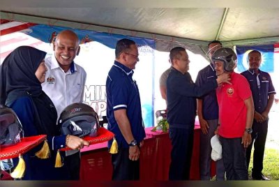 Aedy Fadly (tiga dari kanan) membantu penduduk memakai topi keledar baharu pada Program Santuni Madani di Kampung Alor Senjaya pada Selasa.