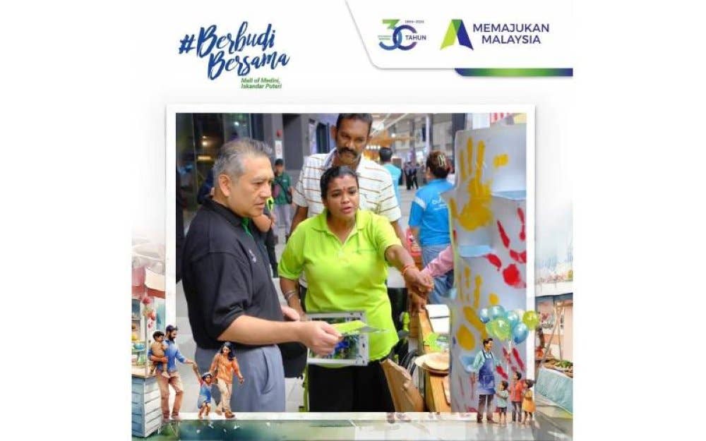 Amirul Feisal (kiri) mendengar penerangan daripada salah seorang wakil pempamer yang menyertai Program #BerbudiBersama di Medini Mall, Iskandar Puteri pada Sabtu.