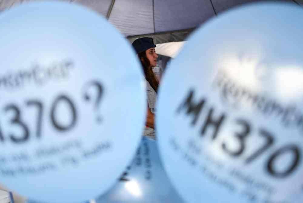 Seorang wanita kelihatan di antara dua belon dengan mesej bertulis 'Ingat MH370?' semasa acara memperingati kehilangan pesawat itu, di Kuala Lumpur 2018.