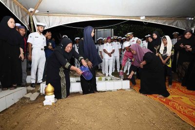 Adjirah menyiram air mawar di atas pusara anaknya yang selamat dikebumikan di Tanah Perkuburan Islam Kampung Terusan pada Jumaat. Foto Bernama