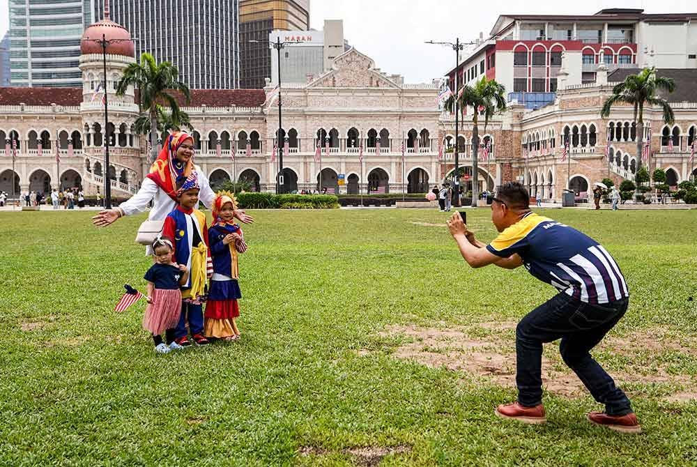 Mohamad Nazrin Zainon Abdidin, 32 (kanan) mengambil gambar isteri Nurizan Jaffor Ghani, 34 (kiri, belakang) dan anak-anaknya yang memakai pakaian bercorak Jalur Gemilang sempena Hari Kebangsaan ke-67 ketika tinjauan di Dataran Merdeka, pada Sabtu. Foto Bernama