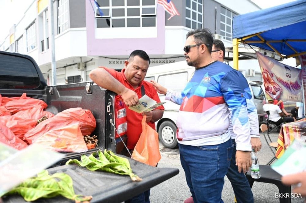 Manndzri (kanan) mengedarkan risalah dan memberikan penerangan mempromosikan Program Tanam Semula bersama RISDA kepada orang ramai.