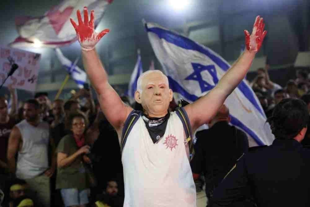 Penunjuk perasaan memakai topeng muka Netanyahu mengangkat tangan seakan-akan berlumuran darah di Tel Aviv.