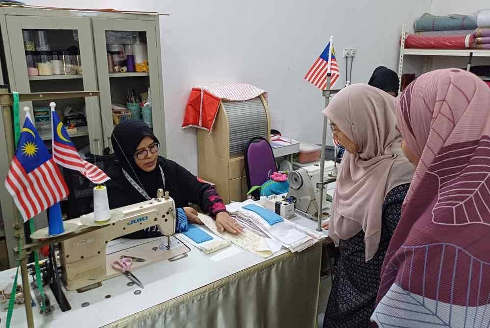 Fuziah (tengah) melihat cara pembuatan tuala wanita ketika meninjau persiapan akhir projek pembuatan kit kebersihan wanita di Teja SKills Tanjung Lumpur.