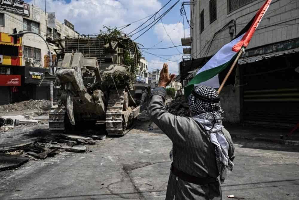 Seorang aktivis Palestin yang memegang bendera kebangsaan cuba menghalang jengkaut milik Israel daripada membinasakan jalan di Jenin.