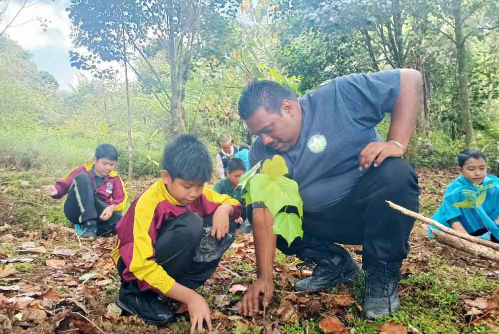 Dilip Martin (kanan) menyantuni seorang pelajar yang turut sama menyertai program penanaman semula pokok dijalankan Persatuan Kesedaran Alam Sekitar Cameron Highlands (Reach) di Pusat Biodiversiti Reach di Gunung Brinchang pada Rabu.
