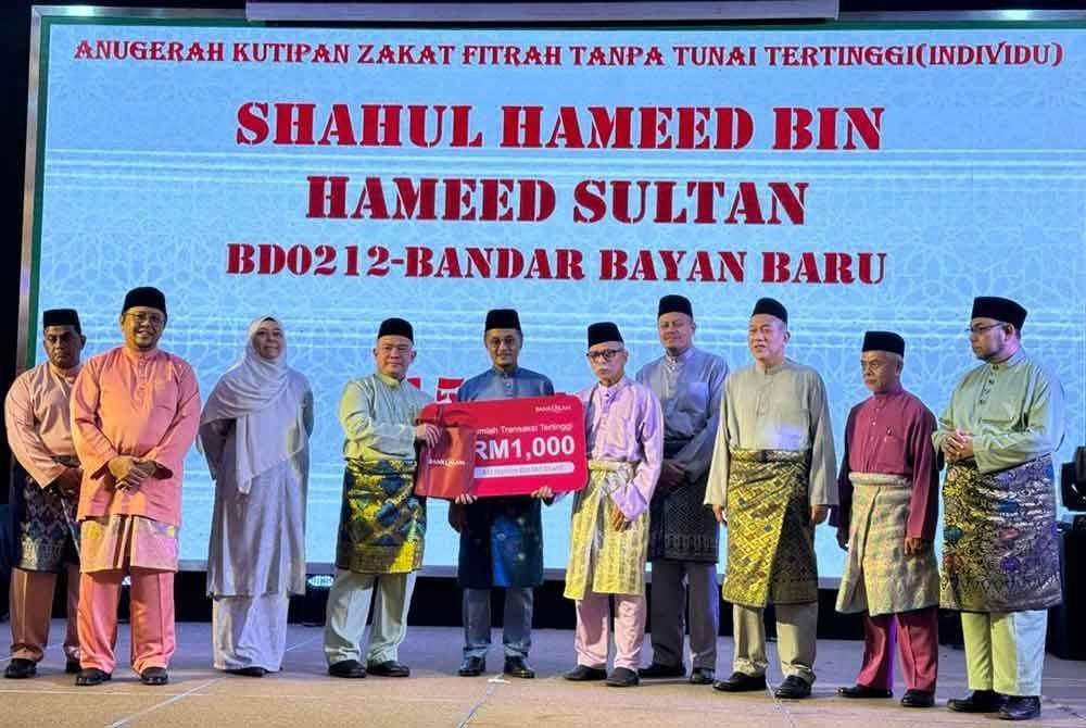 Salah seorang daripada 16 amil zakat fitrah menerima saguhati berjumlah RM1,000 daripada Mohamad (enam daripada kanan).