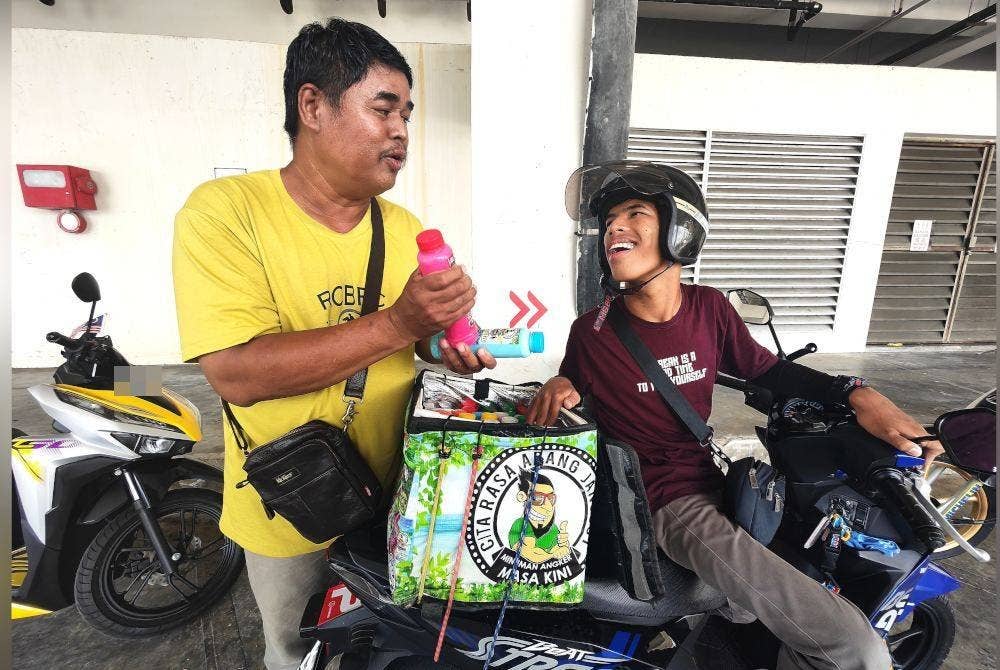 Aniq Fitri bergurau dengan Ros Efendi yang sedang menyusul air di dalam kotak penyimpanan di belakang motosikalnya.