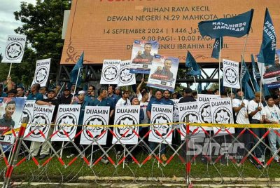 Sepanduk 'dijamin halal' dibawa penyokong PN di luar pusat penamaan calon di Dewan Tunku Ibrahim Ismail, Kluang pada Sabtu.