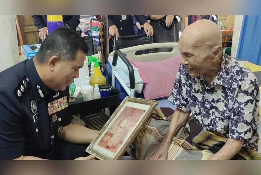 Azli (kiri) melihat potret Besar ketika melawat pesara polis itu di rumahnya di Chabang Tiga, Kuala Terengganu.