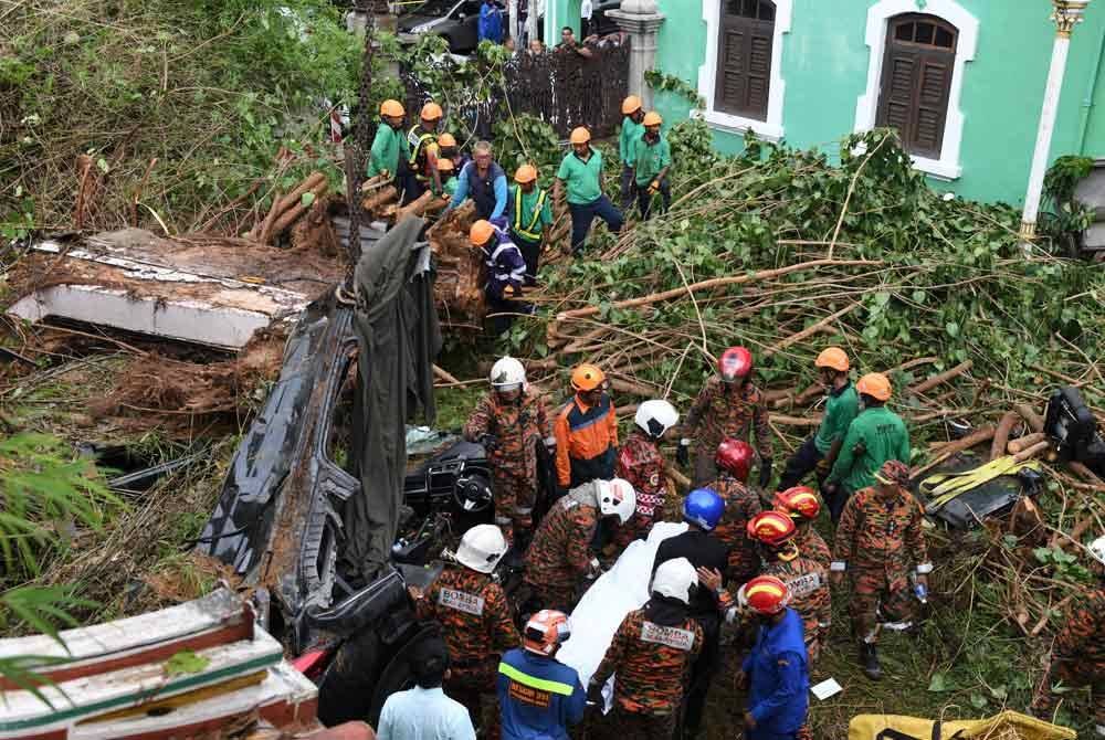 Anggota Bomba dan Penyelamat mengeluarkan satu daripada dua mayat rakyat asing yang maut selepas kereta dinaiki dihempap pokok tumbang di Lebuh Gereja pada Rabu. Foto Bernama