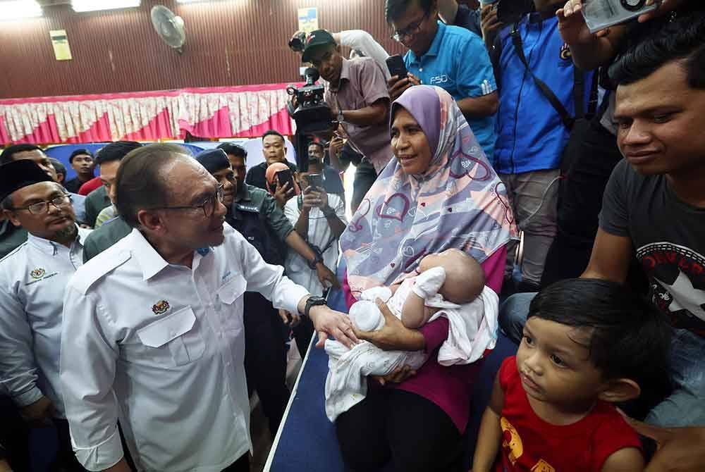 Anwar menyantuni Roshayati Saad yang memangku cucunya Nur Raisha Mikayla yang berusia 38 hari, ketika melawat mangsa banjir di PPS Sekolah Menengah Kebangsaan Agama Kedah. Foto Bernama
