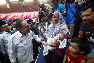 Anwar menyantuni Roshayati Saad yang memangku cucunya Nur Raisha Mikayla yang berusia 38 hari, ketika melawat mangsa banjir di PPS Sekolah Menengah Kebangsaan Agama Kedah. Foto Bernama
