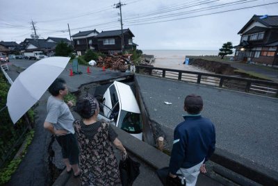 Penduduk tempatan melihat kereta yang terperangkap di jalan yang musnah akibat hujan lebat di Suzu,Ishikawa, Jepun. Foto EPA