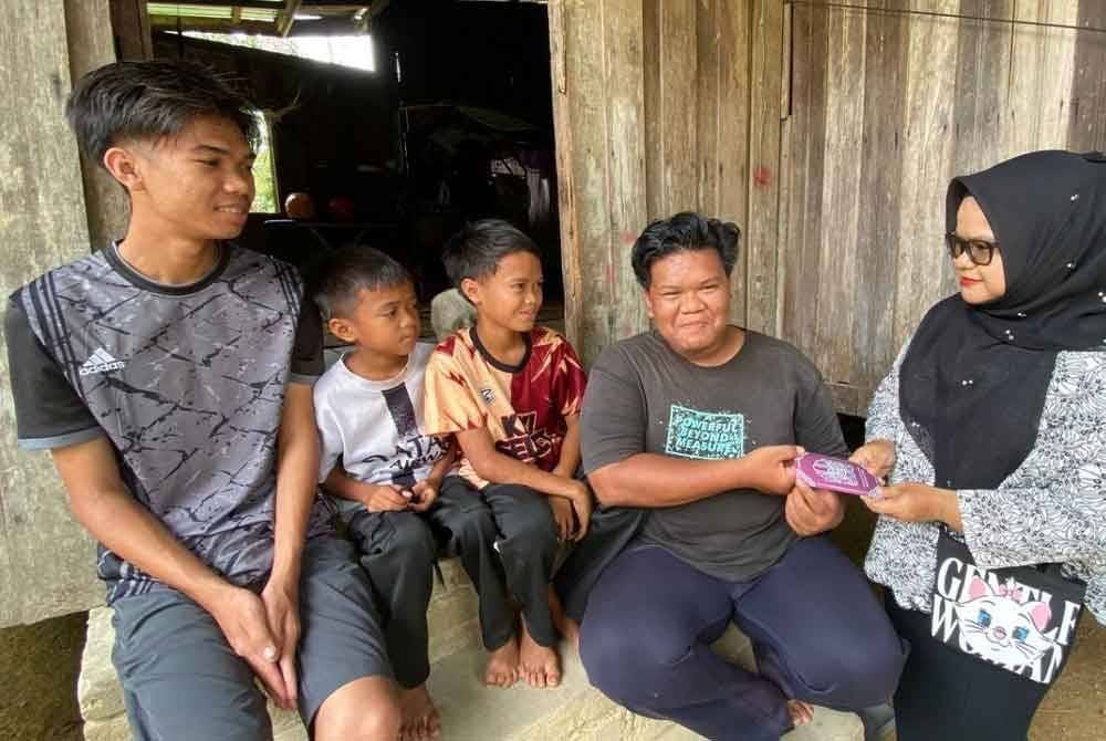 Muhamad Riduan dan adik-adiknya menerima sumbangan Yayasan Nur yang disampaikan Hazelen Liana (kanan) di rumah mereka di Kampung Chuchuh Puteri, Kuala Krai pada Ahad.