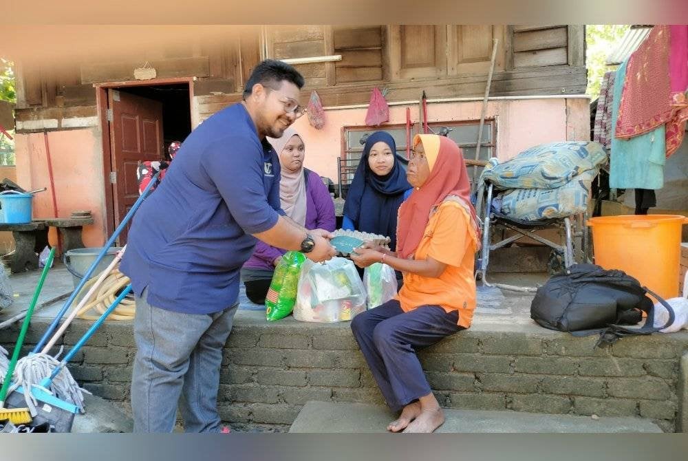 Firdaus (kiri) menyampaikan sumbangan kepada Hasnah selepas membantu membersih rumahnya daripada kesan banjir di Kampung Seberang Pumpong, Bakar Bata, Alor Setar pada Rabu.