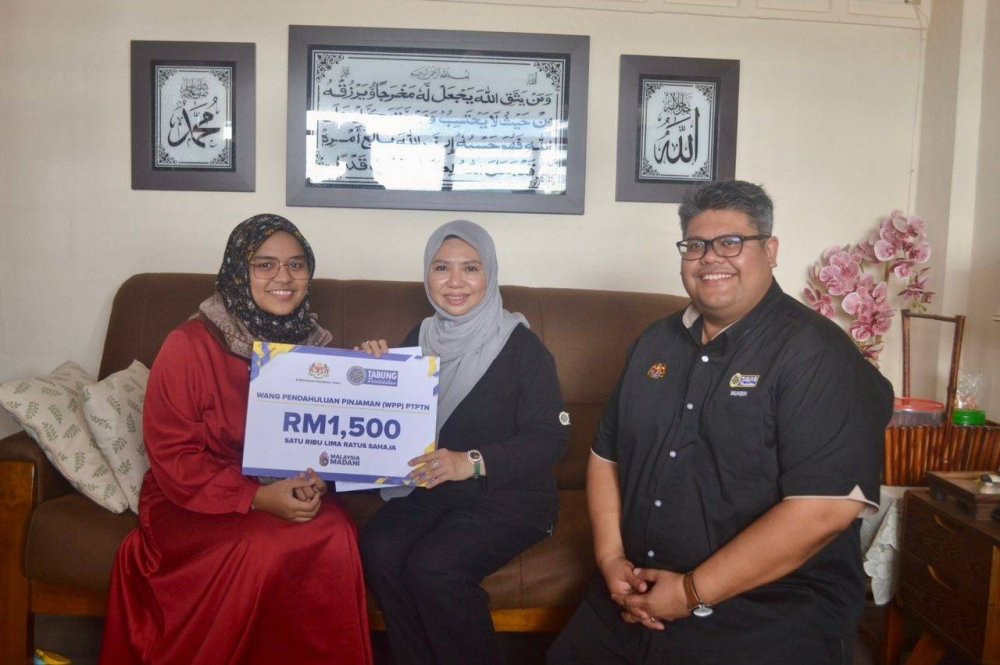 Norliza (tengah) bersama Pengarah Negeri, Pejabat PTPTN Negeri Pulau Pinang, Muhammad Muhsin Abdul Rahman (kanan) menyerahkan replika kad WPP berjumlah RM1,500 kepada pelajar secara walkabout melibatkan tiga buah rumah di Parlimen Bukit Gelugor, Pulau Pinang.