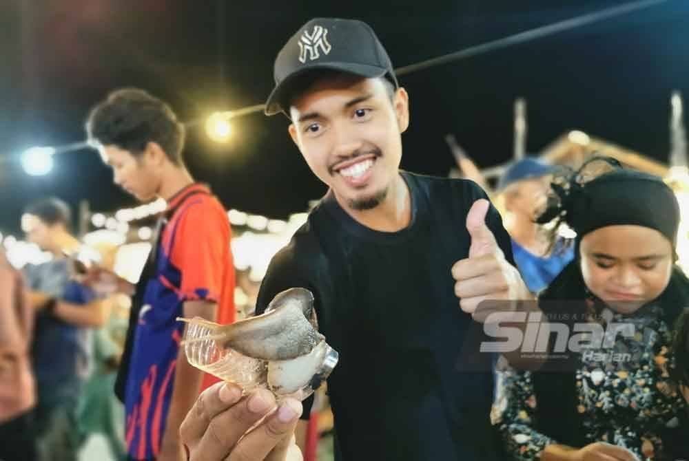 Seorang peserta mempertaruhkan siput babi ketika menyertai pertandingan 'Siputrace' pada malam Khamis.