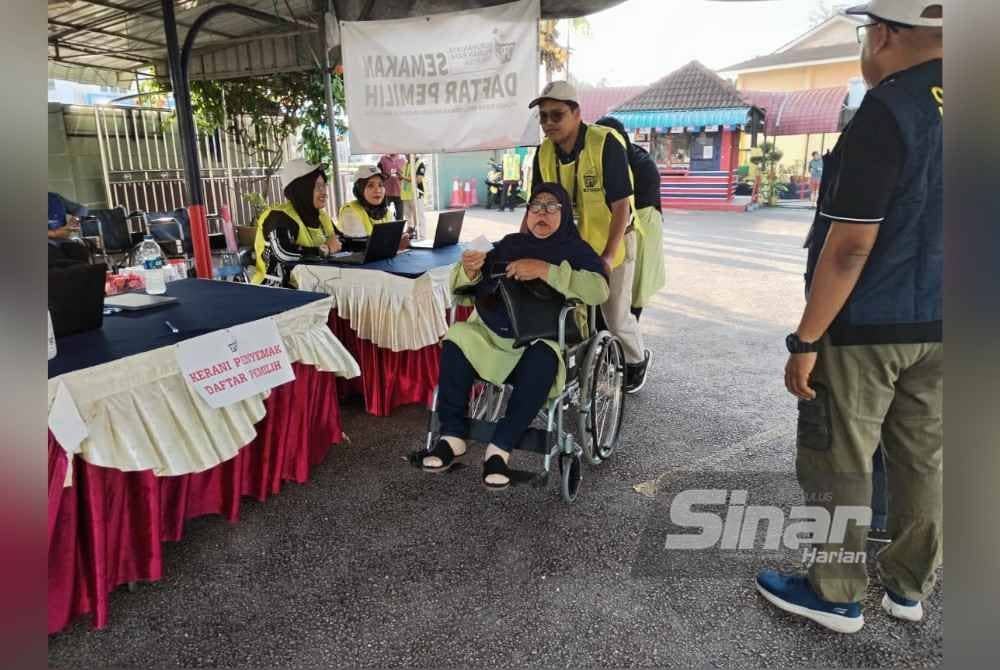 Petugas Suruhanjaya Pilihan Raya (SPR) membantu seorang pengundi yang berkerusi roda di pusat mengundi SMK Sultan Abdul Jalil, Kluang, sempena Pilihan Raya Kecil (PRK) Dewan Undangan Negeri (DUN) Mahkota, pagi ini.