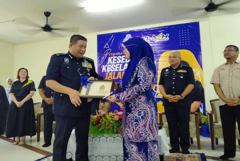 Azizi (kiri) menyampaikan cenderahati kepada Norelawati sempena Program Advokasi Kesedaran Keselamatan Jalan Raya Bersama PDRM dan Flash Express di SMK Dato' Haji Mohd Taib, Chemor pada Isnin.