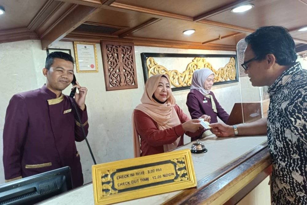 Suaibah (tengah) ketika melayan pelanggan yang sedang mendaftar masuk ke sebuah hotel.
