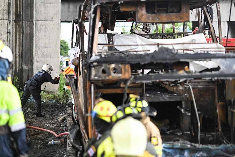 Seorang pegawai polis mengambil gambar ketika dia memeriksa bahagian belakang bas yang terbakar di pinggir Bangkok pada Selasa. Foto AFP