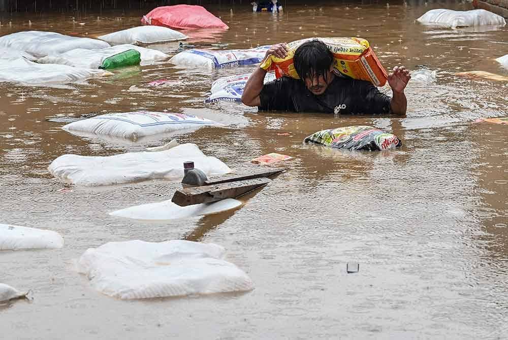 Seorang lelaki membawa guni tepung mengharungi air banjir selepas Sungai Bagmati melimpah berikutan hujan monsun lebat di Kathmandu. Foto AFP