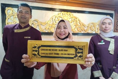 Suaibah (tengah) menunjukkan papan tanda masuk premis hotel di negeri ini bermula jam 3 petang dan keluar pada jam 12 tengah hari.