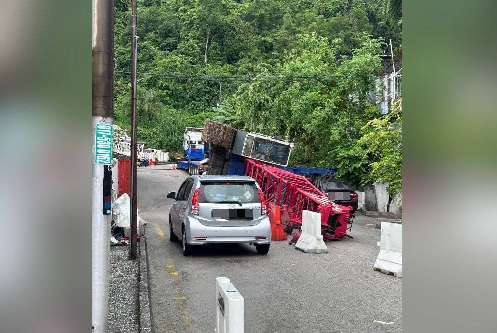 Kren yang dibawa sebuah treler terbalik lalu terkena sebuah rumah dan kereta di kawasan berhampiran. Foto FB Connie