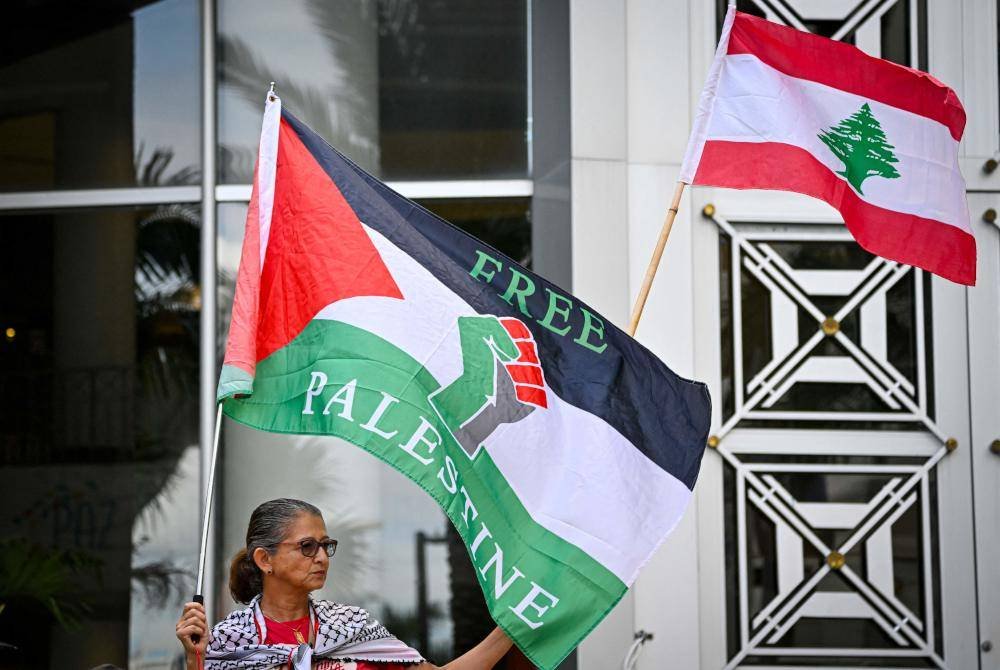 Seorang penunjuk perasaan mengibarkan bendera Palestin dan Lubnan ketika orang ramai berhimpun menyokong Gaza dan Lubnan di hadapan Dewan Bandaraya untuk menandakan satu tahun perang antara Hamas dan Israel di Orlanda, Florida. Foto AFP