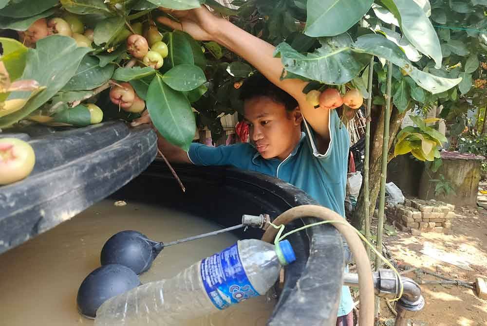 Mohd Nabil menunjukkan tong air yang mengandungi air telaga keruh yang disedut naik melalui paip.