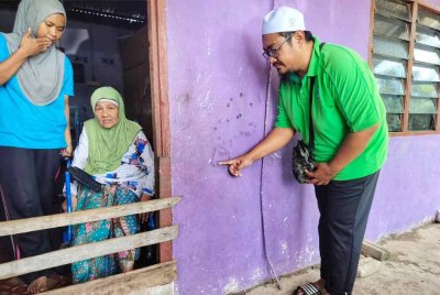 Mohamad Sukor menunjukkan paras air banjir di dinding rumah mereka sambil diperhatikan ibunya.