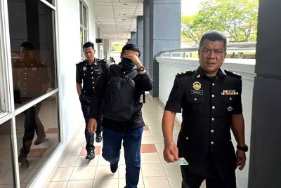 Mohd Firdaus (tengah) diiring pegawai KPDN ketika hadir ke mahkamah.