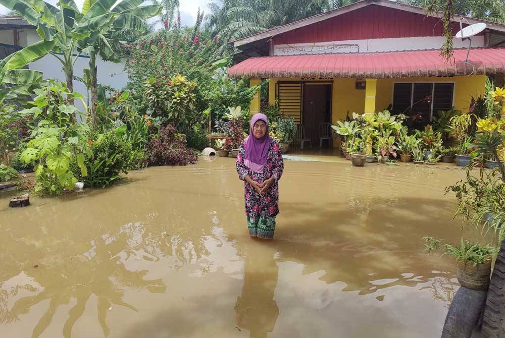 Khatijah meredah banjir di laman rumahnya di Kampung Tanjung Medan pada Jumaat.